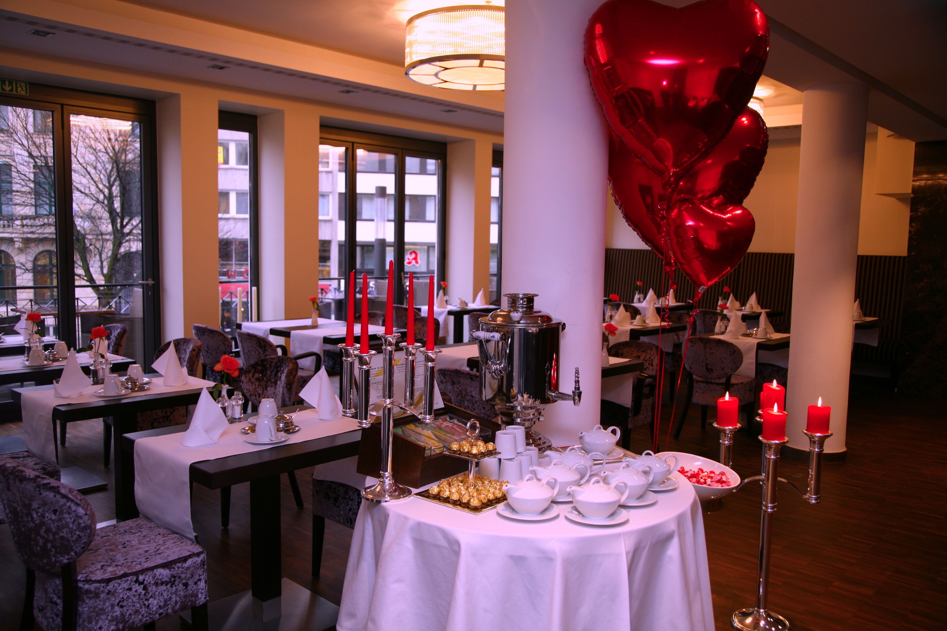 A dining area with tables set for a meal, candles, and a heart-shaped balloon decoration.