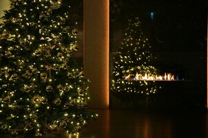 Un albero di Natale decorato con luci e ornamenti, un camino con fiamme vive e un pilastro in una stanza scarsamente illuminata.
