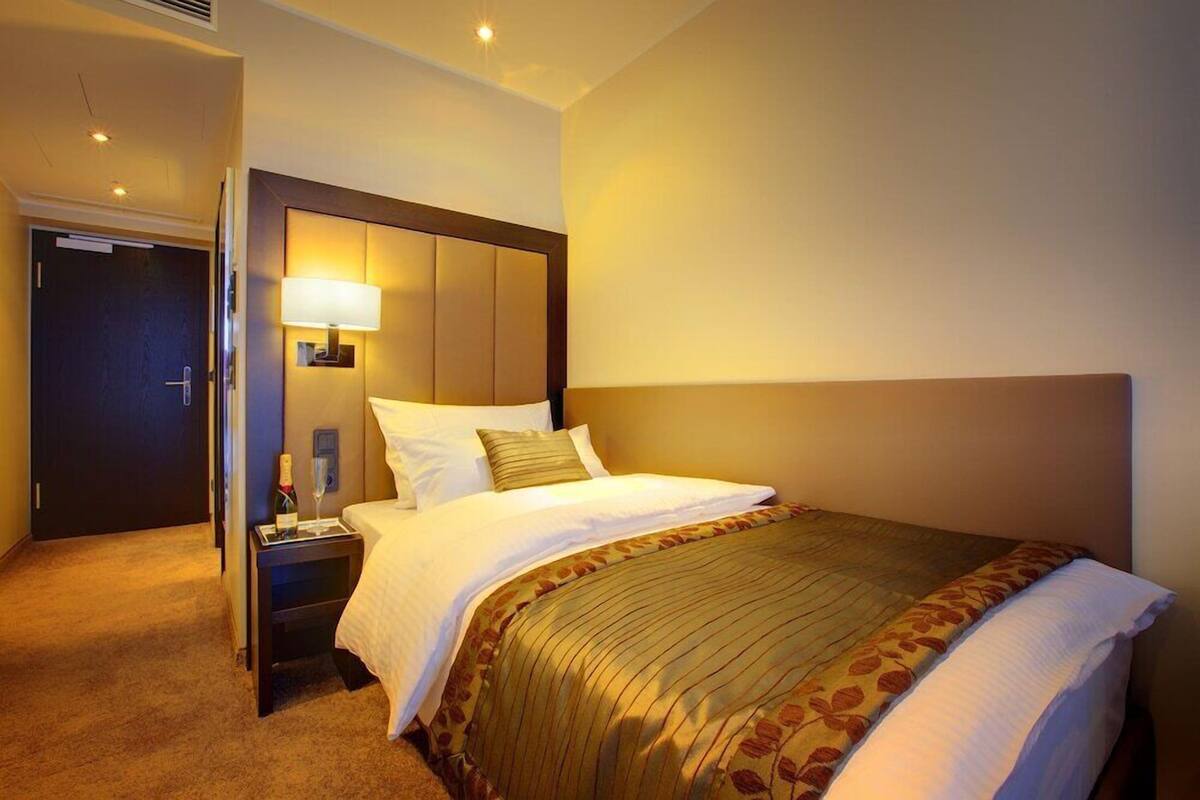 A hotel room with a large bed, a nightstand with a lamp, a door, and a carpeted floor.