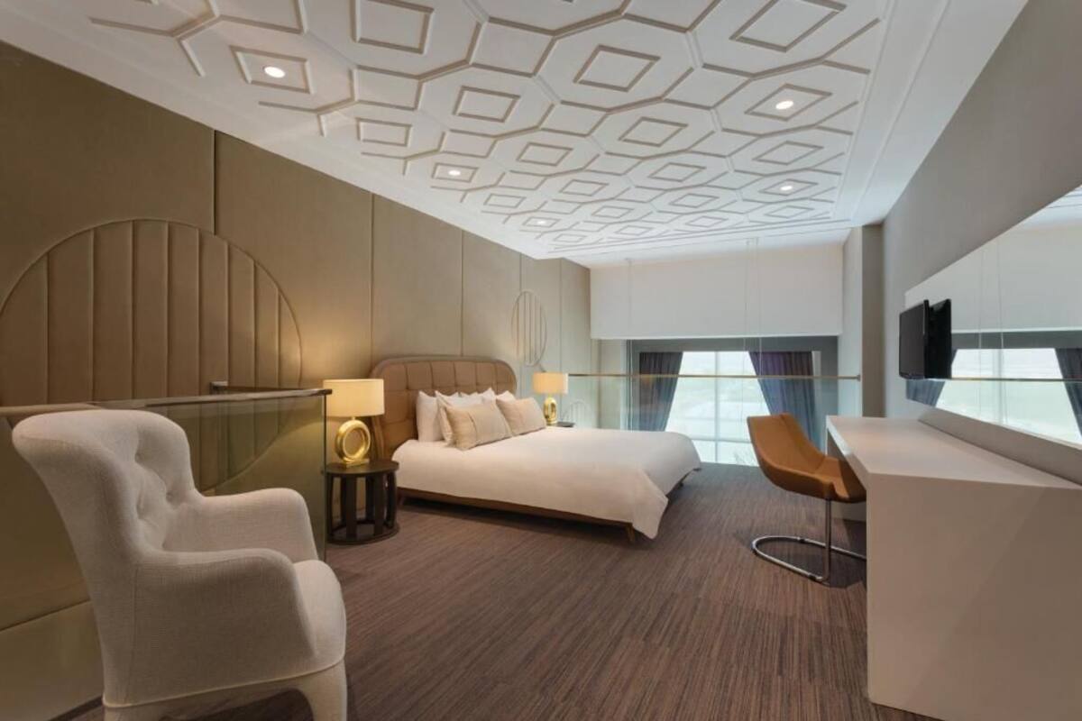 Ein modernes Hotelzimmer mit einem großen Bett, einer Sitzecke mit einem Sessel, einem Schreibtisch und einem Fernseher.