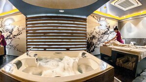 A spa room with a large bathtub, two massage tables, and a decorative wall with a tree design.