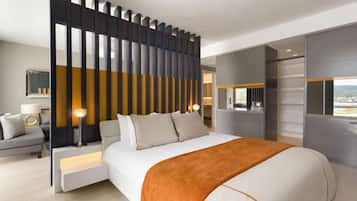 Quarto de hotel moderno com uma cama grande, mesa de cabeceira, escrivaninha e vista para a cidade.