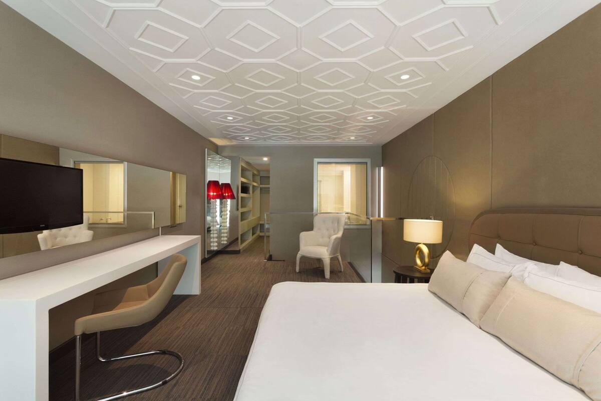 Ein Hotelzimmer mit Bett, Schreibtisch, Stuhl, Fernseher, Lampe und Kleiderschrank.