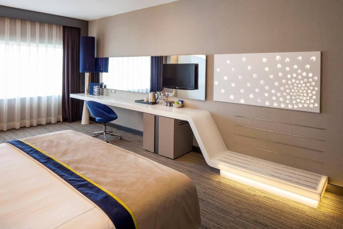 Ein Hotelzimmer mit Bett, Schreibtisch, Sessel, Fernseher und einer Wanddekoration.