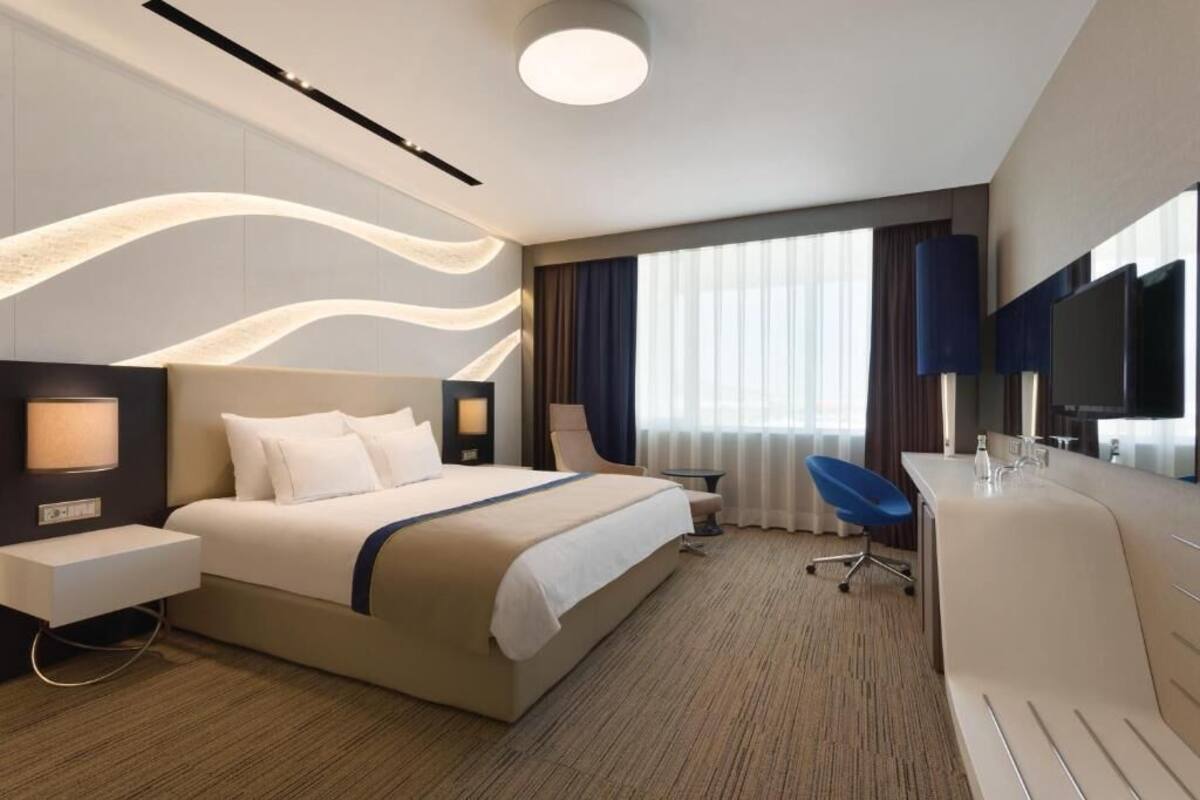 Ein modernes Hotelzimmer mit einem großen Bett, einem Schreibtisch, einem Sessel und einem Fernseher.