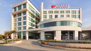 A modern hotel with a curved facade, large windows, and a prominent sign for Ramada Hotel & Suites.
