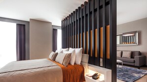 A modern bedroom with a large bed, a bedside table with a phone, a sofa, and a patterned rug.