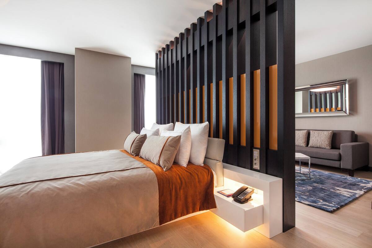 Ein modernes Schlafzimmer mit einem großen Bett, einem Nachttisch mit Telefon, einer Couch und einem gemusterten Teppich.