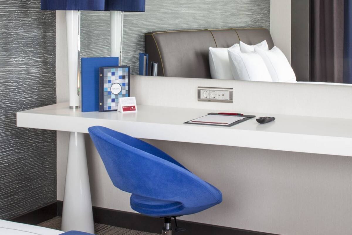 Ein Hotelzimmer mit Schreibtisch, Stuhl, Bett, Lampe und Tablett mit Tasse und Keks.