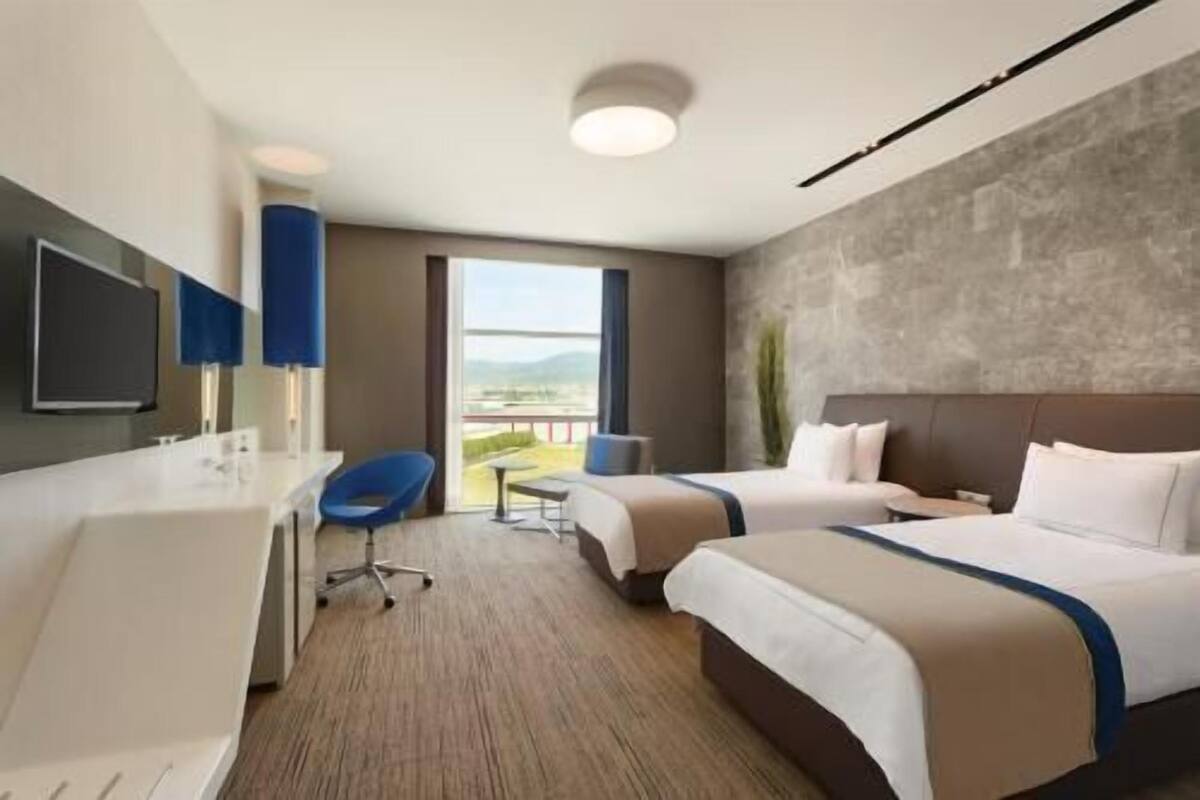 Ein Hotelzimmer mit zwei Betten, einem Schreibtisch, einem Stuhl und einem großen Fenster mit Blick.