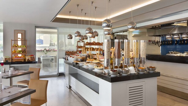 A modern breakfast bar with a variety of food items, a seating area with chairs, and a kitchen area with utensils hanging above.