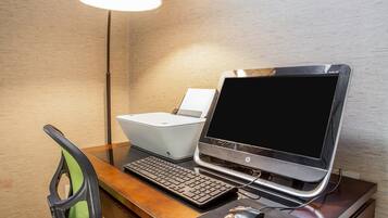 Una habitación de hotel con un escritorio de madera, una computadora portátil, un teclado, un ratón y una lámpara.