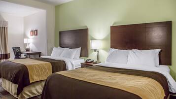 A hotel room with two beds, each with a brown headboard, white bedding, and a beige accent on the bedspread. There is a small table with a lamp, a chair, and a telephone on the nightstand.