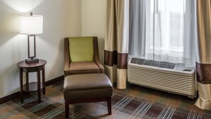 A hotel room with a single chair, a standing lamp, a window with curtains, and an air conditioning unit. - Comfort Inn Lexington South (Nicholasville)