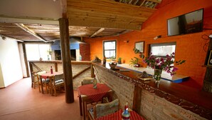 A rustic restaurant with wooden tables and chairs, brick walls, and a TV mounted on the wall.