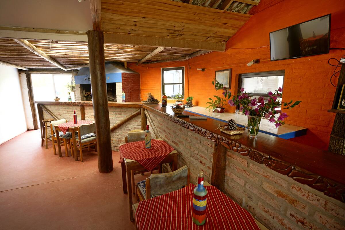 A rustic restaurant with wooden tables and chairs, brick walls, and a TV mounted on the wall.