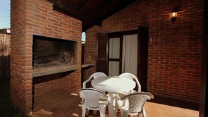 An outdoor patio with a brick oven, white plastic chairs, and a table.