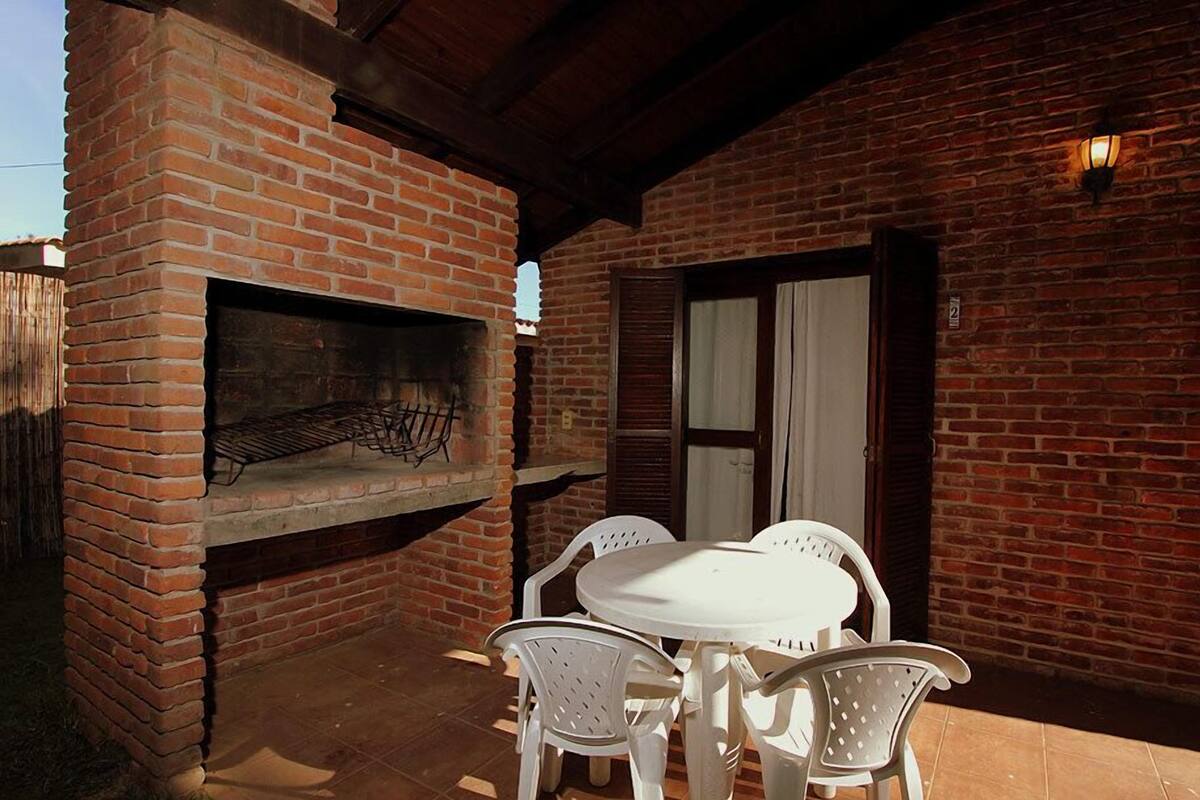 An outdoor patio with a brick oven, white plastic chairs, and a table.