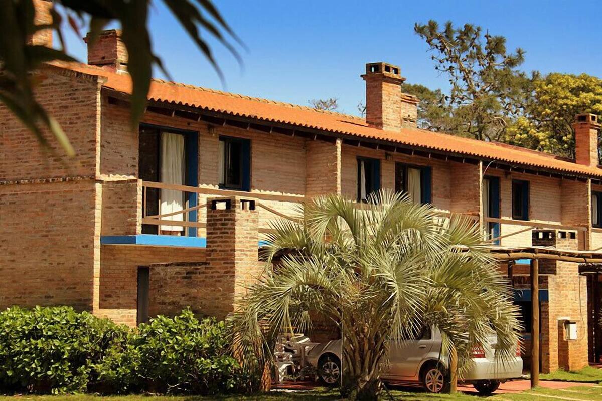 A two-story brick building with a red-tiled roof, multiple windows, and a car parked in front.