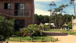 A two-story brick building with a balcony, surrounded by greenery and a clear sky.