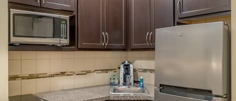 Una cocina compacta con armarios marrón oscuro, un refrigerador de acero inoxidable, un microondas y un lavavajillas.