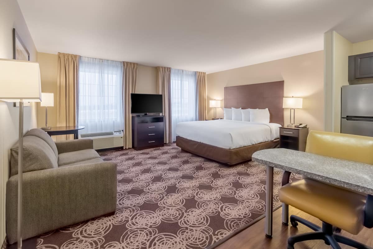 A hotel room with a bed, a desk, a chair, a television, and a refrigerator.