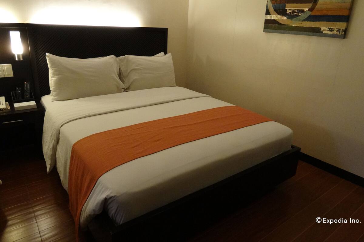 A hotel room with a large bed, a nightstand with a lamp, and a painting on the wall.