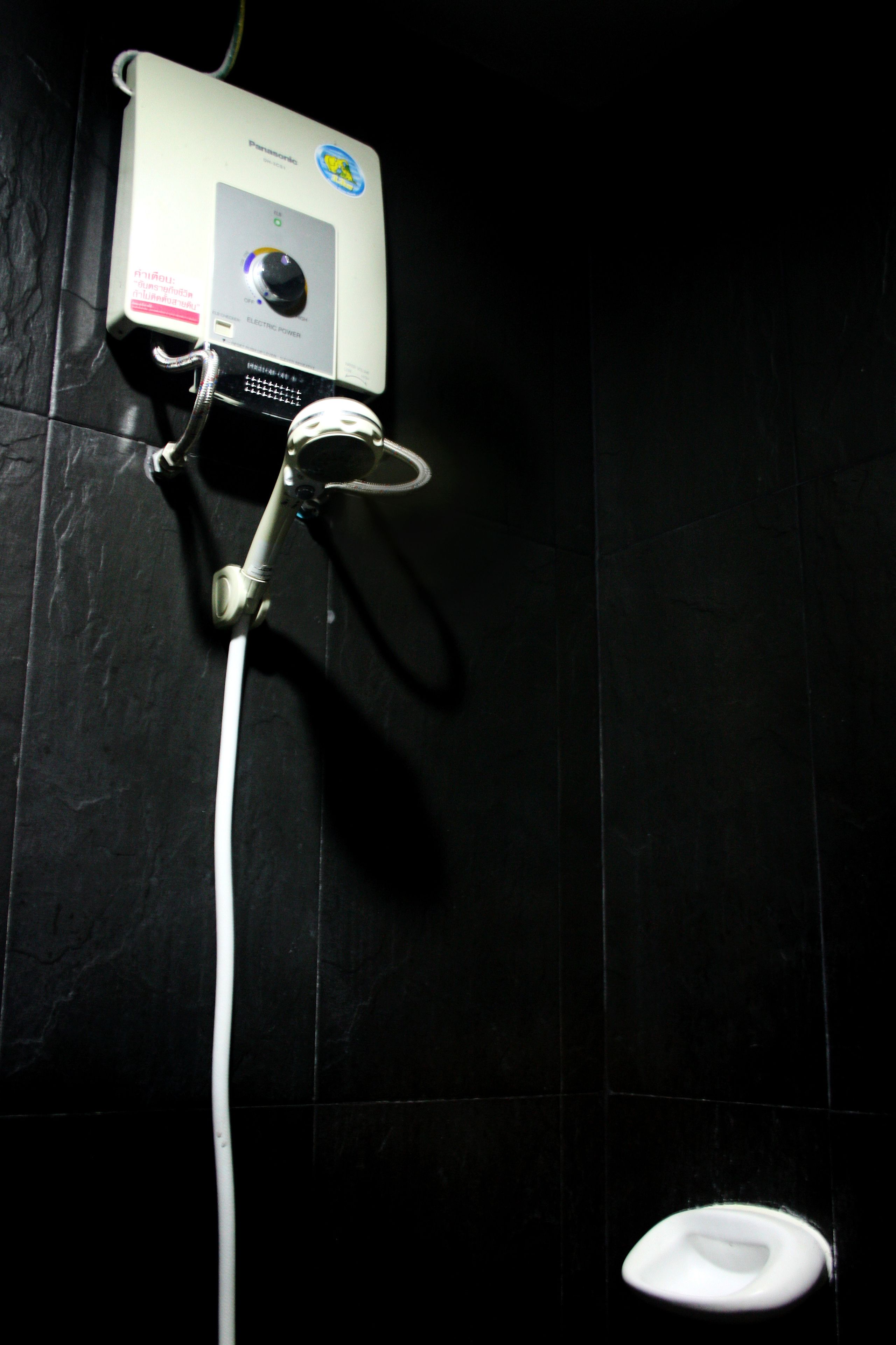 A bathroom with a handheld showerhead, a wall-mounted electric heater, and a toilet.