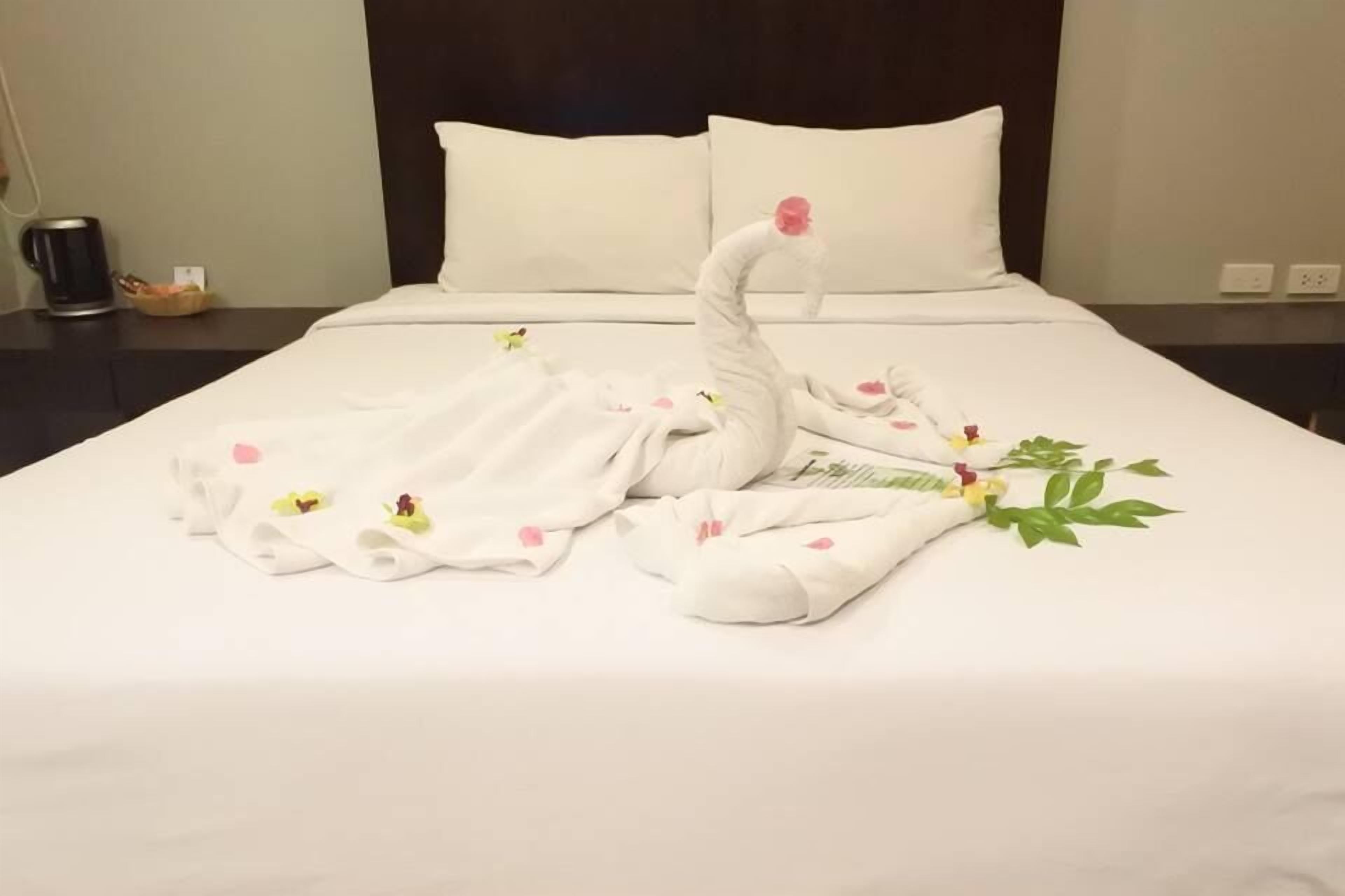 A neatly made bed with a swan towel arrangement, including a swan head with a pink flower and a swan tail with a green leaf.