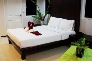 A neatly made bed with white linens, a heart-shaped towel, and a red cloth on the left side. There is a green plant on a table to the right. - Baannueng (Kathu)