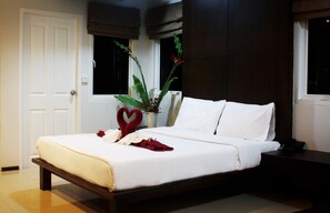 A neatly made bed with white linens, a heart-shaped decoration, and a vase with green plants. - Baannueng (Kathu)