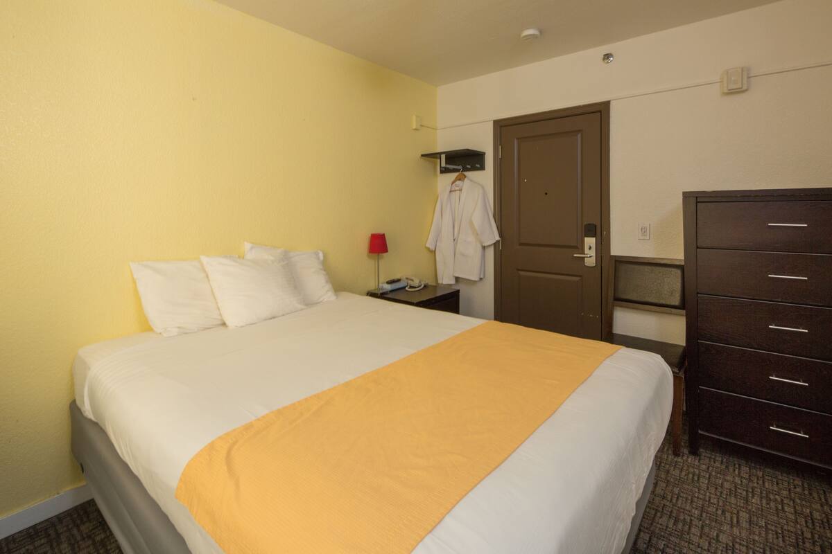 A hotel room with a bed, a dresser, a door, and a coat rack.