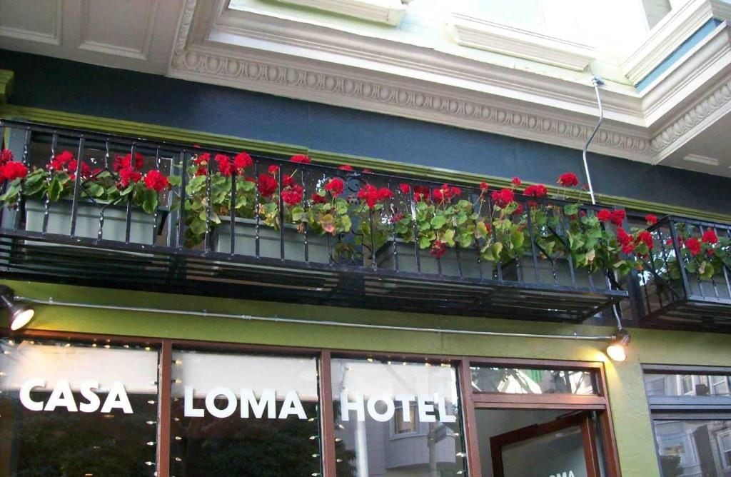 Entrada de un hotel con un balcón decorado con flores rojas y el nombre 'CASA LOMA HOTEL' exhibido en las ventanas.