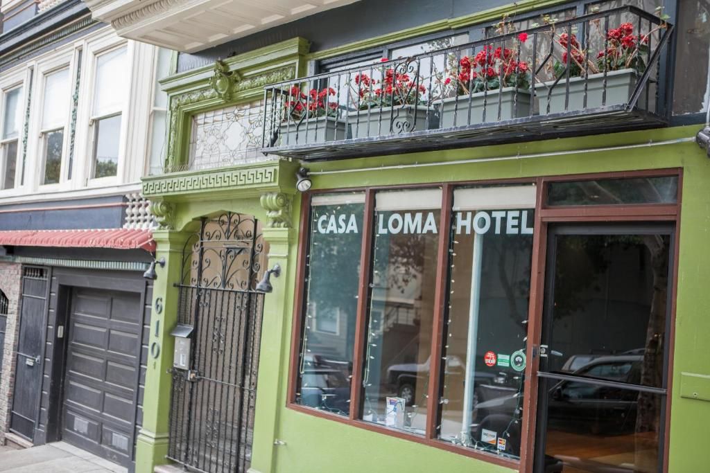 A green building with a balcony with red flowers, a large window with the words 'CASA LOMA HOTEL' on it, and a black gate.