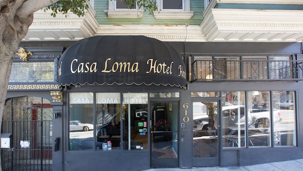 The exterior of Casa Loma Hotel with a black awning and a large glass entrance.