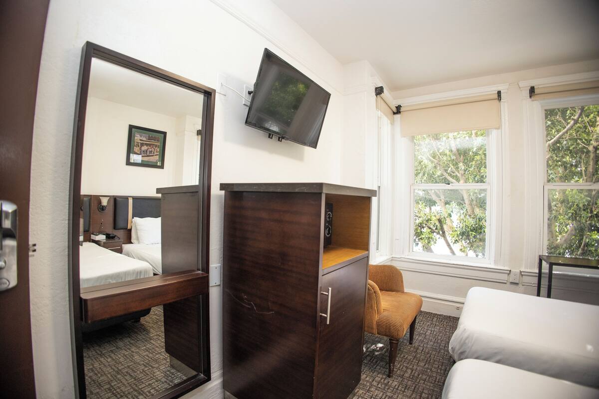 A hotel room with a bed, a dresser, a television, and a window with a view of trees.