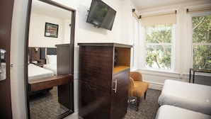 A hotel room with a bed, a dresser, a television, and a window with a view of trees.