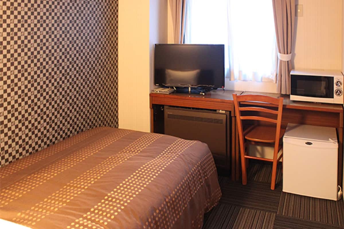 Ein Hotelzimmer mit Bett, Schreibtisch, Fernseher, Mikrowelle und Kühlschrank.