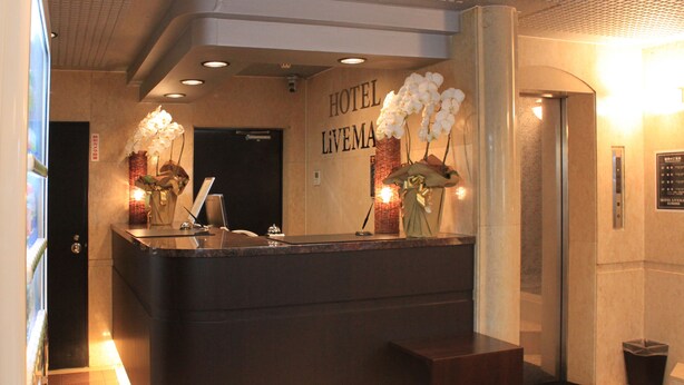 Een hotel receptiebalie met een donker aanrecht, twee witte orchidee vazen, en een 'HOTEL LIVING' bord.