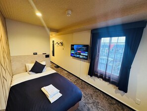 Une chambre d’hôtel avec un lit, un téléviseur à écran plat fixé au mur et une fenêtre avec des rideaux.