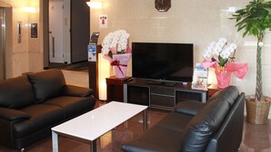 Een hotellobby met een flatscreen televisie, leren banken, een receptiebalie en een potplant.