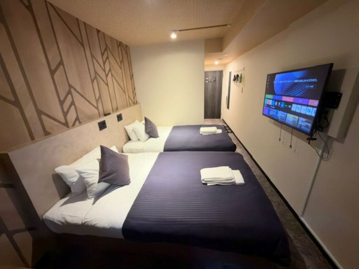 Habitación de hotel con dos camas, un televisor de pantalla plana montado en la pared y un diseño de pared con motivos.