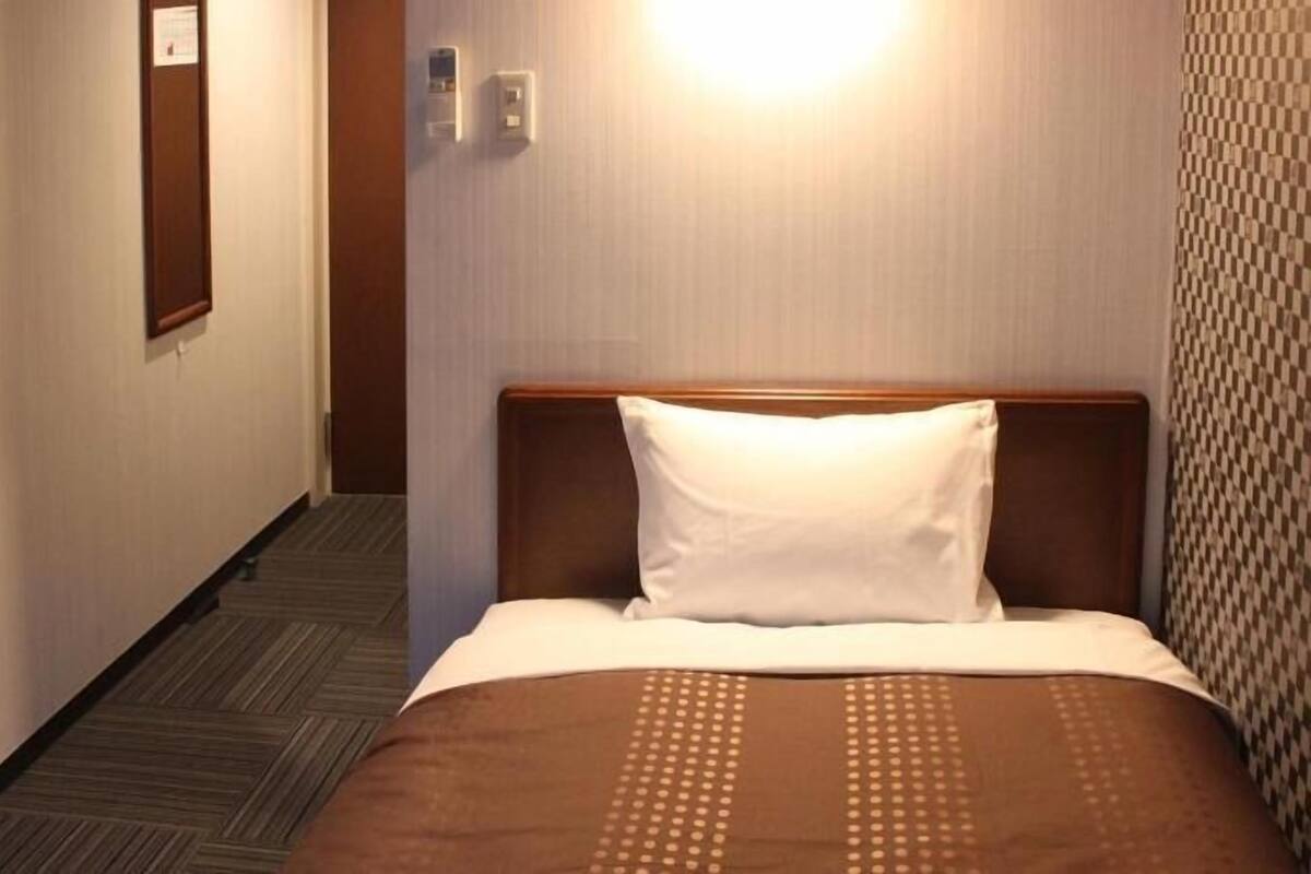 Ein Hotelzimmer mit Bett, Teppichboden, Wandleuchte und Tür.