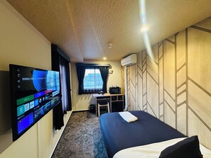 A hotel room with a bed, a desk, a television, and a window with curtains.
