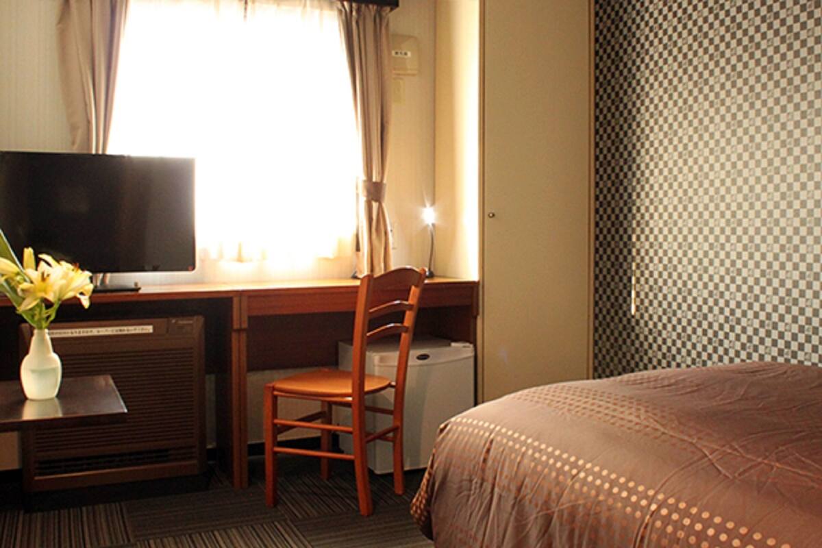 Ein Hotelzimmer mit einem Bett, einem Schreibtisch mit Computer, einem Sessel und einem Fernseher.