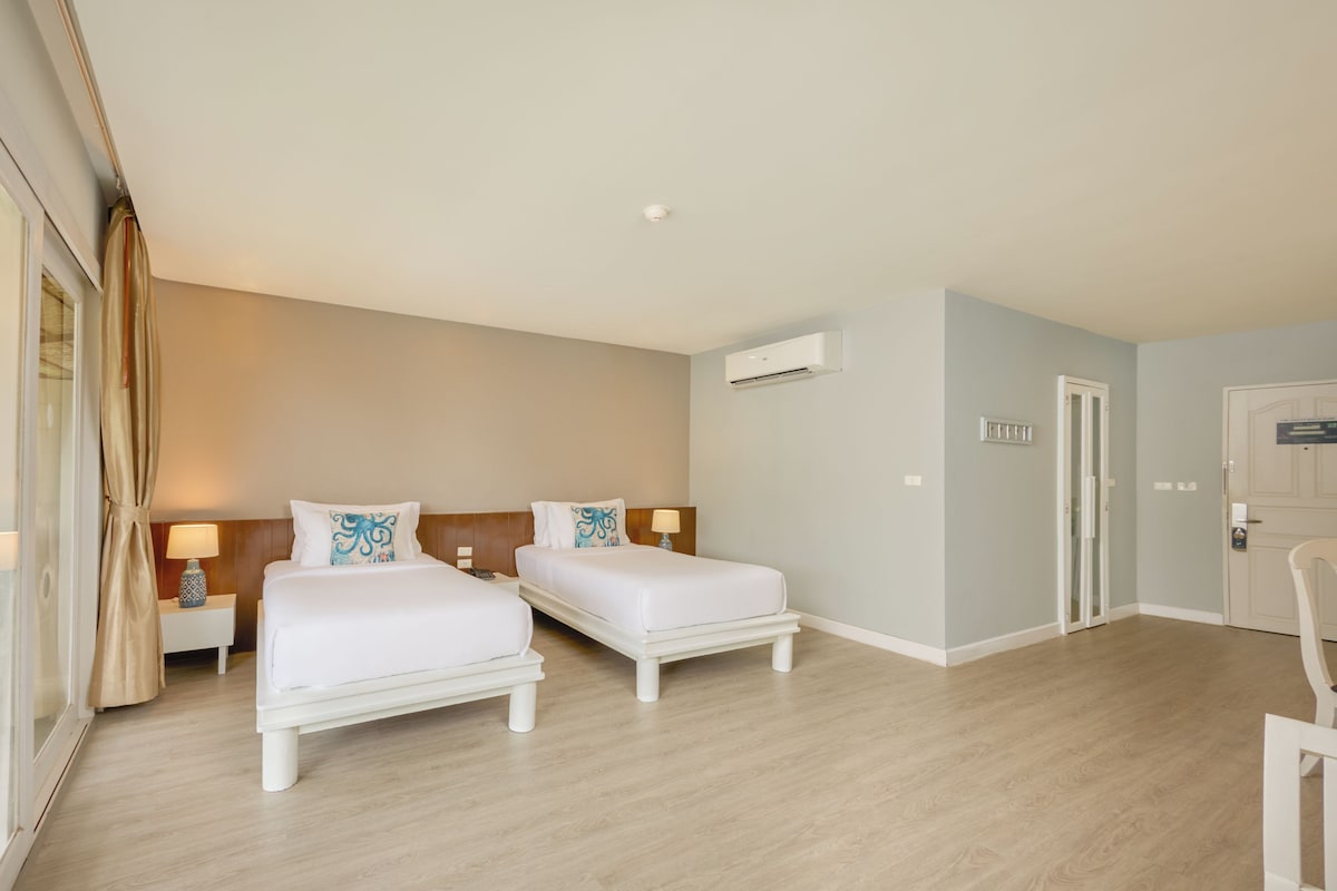 Habitación de hotel con dos camas, un escritorio, una silla y una ventana con cortinas.
