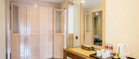 A hotel room with a wooden floor, a wooden desk with a tray holding cups and a bottle, and a large mirror above the desk.
