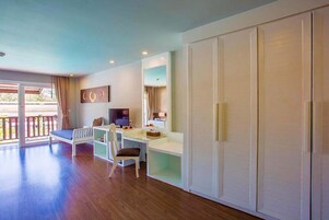 Una habitación con piso de madera, un escritorio blanco con una silla, un televisor y un armario grande.