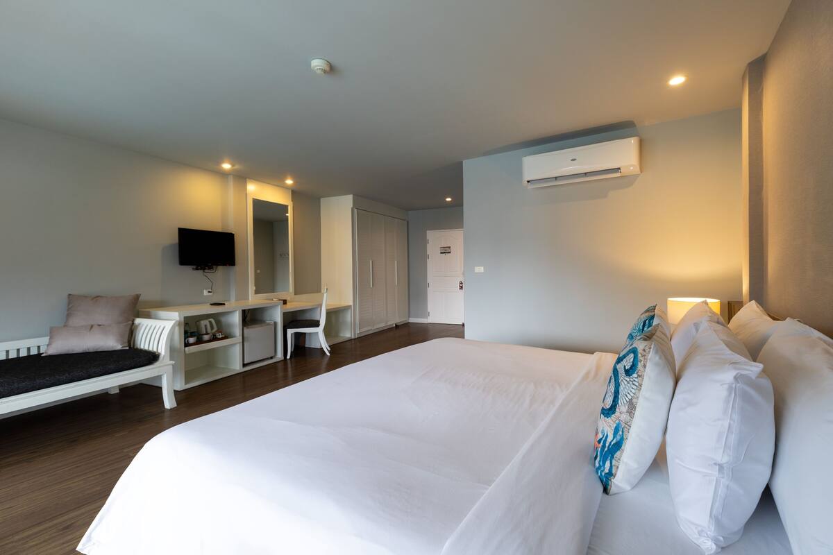 Quarto de hotel moderno com uma cama grande, uma escrivaninha, uma cadeira, uma televisão de tela plana e um ar condicionado.