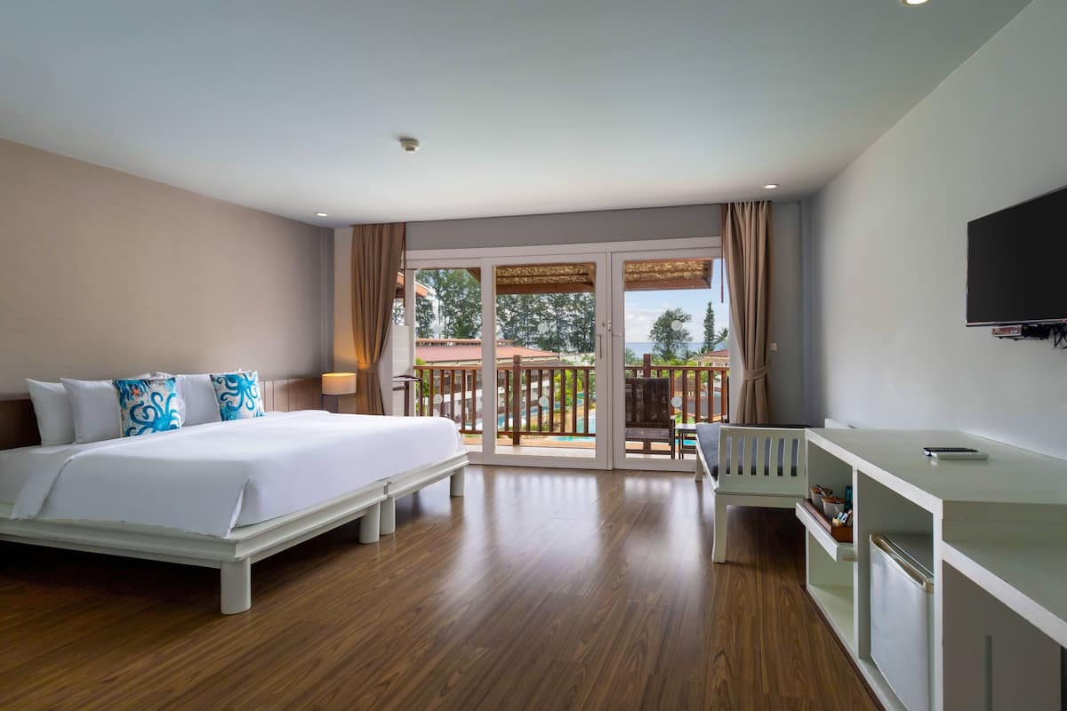 Quarto de hotel com cama, escrivaninha e varanda com vista para o exterior.